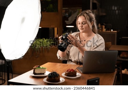 Smiling female food photographer with laptop computer and camera photographing cakes in cafe. Blogging and profession concept. Copy space
