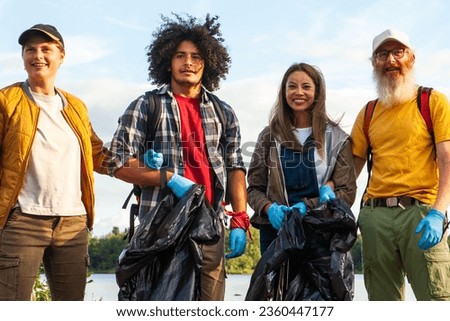 A multiracial group of friends, spanning different ages, comes together in the heart of nature, armed with rubber gloves and garbage bags, ready to embark on a mission to clean up the environment Royalty-Free Stock Photo #2360447177