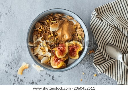 Multigrain wholewheat breakfast cereals with fig, coconut chips, peanut butter and pistachio, top view. Vegan breakfast concept. Royalty-Free Stock Photo #2360452511