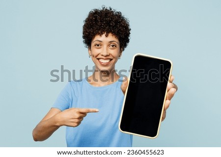 Young woman of African American ethnicity wear t-shirt casual clothes hold in hand use point finger on mobile cell phone with blank screen workspace area isolated on plain pastel light blue background