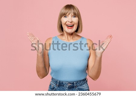 Elderly overjoyed excited fun cool blonde woman 50s years old she wears blue undershirt casual clothes look camera spread hands isolated on plain pastel light pink background studio. Lifestyle concept