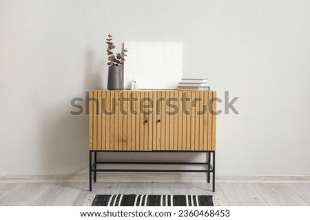 Vase with eucalyptus branches and books on wooden cabinet near white wall Royalty-Free Stock Photo #2360468453