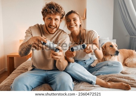 Young couple in love playing video games while sitting on the sofa in the bedroom, having fun and enjoying each other on their weekends.