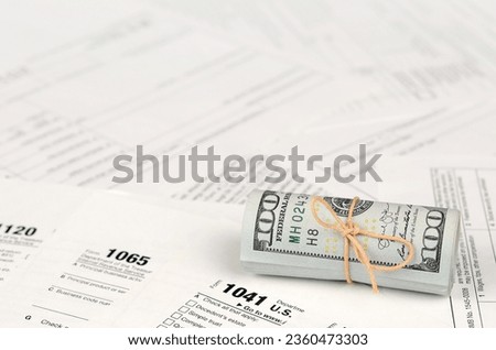 Tax forms lies near roll of hundred dollar bills. Income tax return. Time to pay taxes concept. 1040 1041 1120 and 1065 empty blank forms Royalty-Free Stock Photo #2360473303