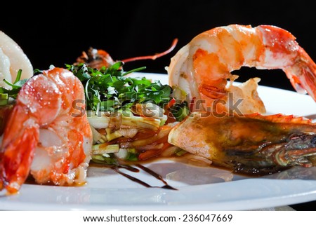 macro prawns lined with herbs on a white plate on a black background studio