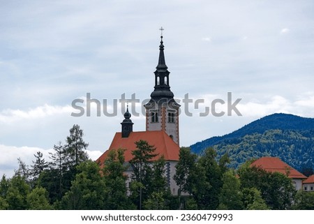 Lake Bled with close-up of church on an island and woodland in the background on a cloudy summer day. Photo taken August 8th, 2023, Bled, Slovenia.