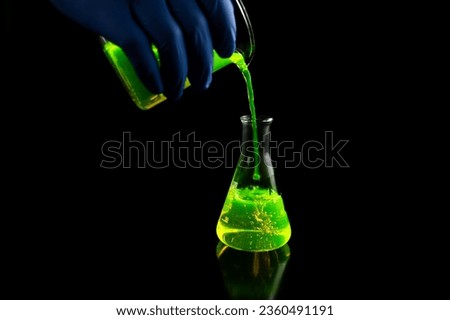 A research scientist experimenting with a green fluorescent droplets in a glass conical flask in dark biomedical laboratory for health care medicine development. Copy space black background Royalty-Free Stock Photo #2360491191