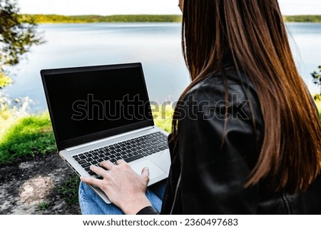 A young freelance woman working outdoors with laptop sitting in nature. Concept of freelancer lifestyle.