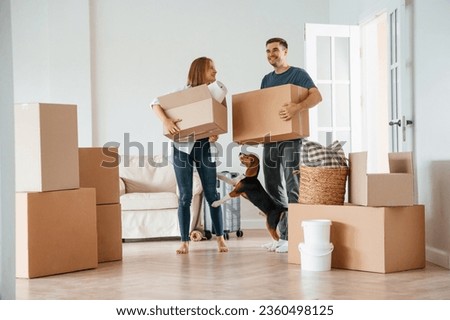 Two boxes in hands. Young couple with dog are moving to new home. Royalty-Free Stock Photo #2360498125