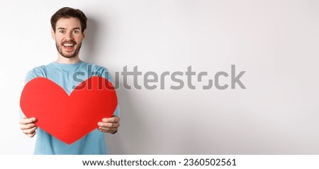 Relationship and people concept. Handsome man give valentines heart to you, smiling and saying I love you at camera, standing over white background.