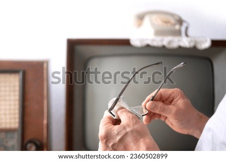 male hands cleaning reading glasses to watch Old-Fashioned retro analog TV 1960-1970, stylish Retro Technology in Everyday Life Royalty-Free Stock Photo #2360502899