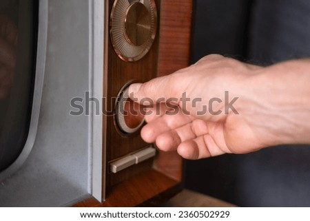 male Hand turns on TV power button, adjusts volume control old retro analog TV, entertainment, Technologies of Past Decades Nostalgia, leisure essential life older individuals, Technology 1960-1970 Royalty-Free Stock Photo #2360502929
