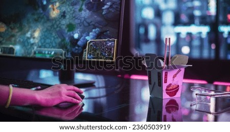 Close Up on Asian Takeaway Food Container on the Table of an Anonymous Gamer Girl Playing Video Games on a Computer. Delivery Service in a Technologically Advanced Room with Futuristic Neon Background