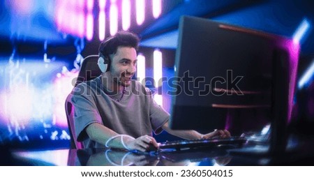 Portrait of a Happy Young Man in Headphones Talking with Friends Online on a Computer. Stylish Streamer or Video Gamer Playing Games and Chatting with Internet Followers in a Futuristic Neon Studio