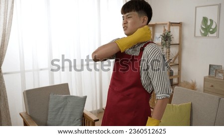 asian cleaning male suffering a sudden pain in his shoulders is moaning and massaging the muscles with grimacing face while using hoover at home Royalty-Free Stock Photo #2360512625