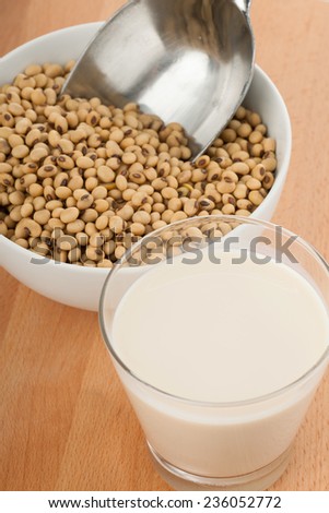 Soy milk in glass with soybeans and  transfer scoop in bowl  on wood table