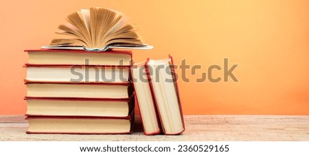 Composition with hardback books, fanned pages on wooden deck table and orange background. Books stacking. Back to school. Copy Space. Education background