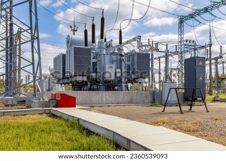 Three-phase high-voltage transformer of high electrical power at a substation against the blue sky. Royalty-Free Stock Photo #2360539093