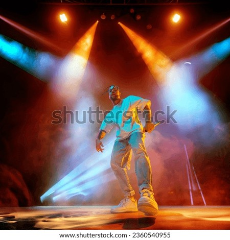 Rap musician. Young artistic man with dreads performing on stage over multicolored neon lights. Concert at night club. Concept of music, performance, art, talent, nightlife, joy, party, lifestyle, ad Royalty-Free Stock Photo #2360540955