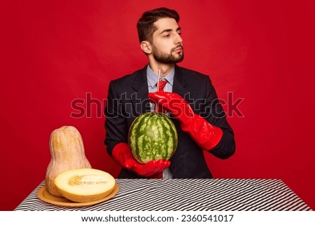 Stylish man in suit sitting at table in red rubber gloves, drinking watermelon, eating melon and pumpkin over red background. Concept of food, creativity, party. Pop art photography. Copy space for ad
