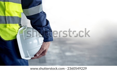 Safety workwear concept. Male hand holding white safety helmet or hard hat. Construction worker man in protective suit and reflective green vest standing with building concrete floor in the background Royalty-Free Stock Photo #2360549229