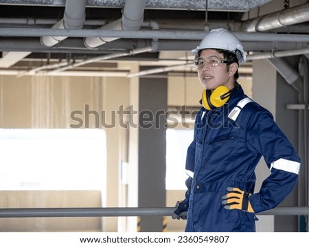 Portrait of Asian confident man construction worker or male maintenance engineer with protective suit, earmuffs, safety helmet and goggles looking away while standing at construction site Royalty-Free Stock Photo #2360549807