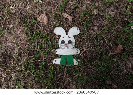 A flat wooden figurine of a sad bunny lies on the ground
