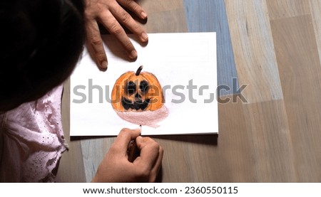 A high-angle shot of a child's hand-drawn pumpkin picture for Halloween, with sunlight shining into the room.