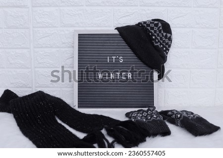 It's Winter text decorate with black woolen scarf, knitted mittens and beanie