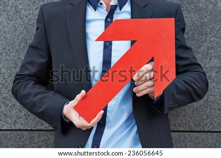 Hands of businessman holding big red arrow pointing up