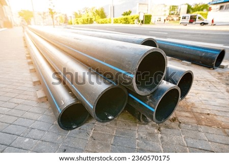 HDPE polyethylene pipes. Black pipe for water supply on pavement. HDPE pipes, plastic pipes lie on the pavement ready for installation and improvement of the water supply system. Royalty-Free Stock Photo #2360570175