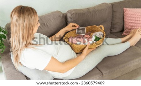 A pregnant woman looks at baby cloth and an ultrasound photo. Selective focus. Cute.