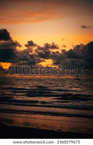 Small sail boat on the sea with a dramatic cloudy yellow and orange sunset over the water