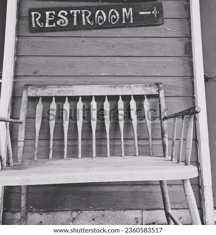 Old wooden bench under restroom sign black and white