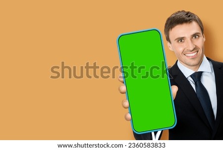 Smiling young business man, show, cell phone, mobile smartphone. Happy businessman hold cellphone green chroma key screen, isolated over brown beige background. Sale ad advertisement
