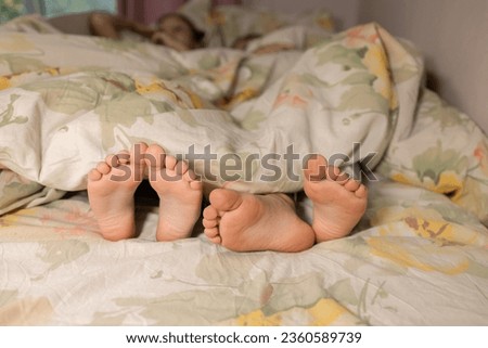 two children sleep in bed. bare, clean feet of siblings, lying side by side under same blanket on the bed. morning relaxation, cozy rest, childish tenderness, family joy. cute pictures of baby feet
