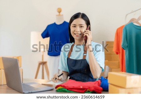 Young Asian business owner talking on smartphone and taking order. Asian female entrepreneur working at home office confirming the order on phone.