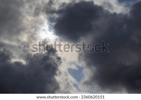 zenith pointed incoming storm cloudscape with heavy clouds and sun between them, full-frame real life photo.