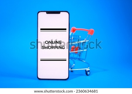 Horizontal photo of a white screen phone next to a shopping cart with text ONLINE SHOPPING on it or a random text of your choice isolated on blue background.