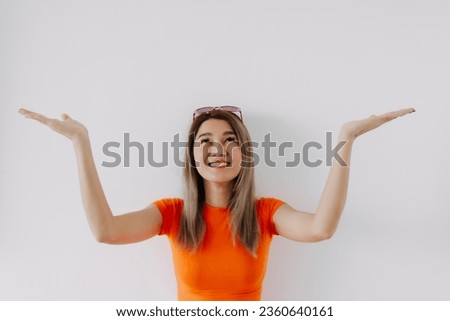 Happy asian Thai woman wear orange shirt , presenting offering and recommending at empty space above her head.