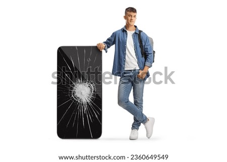 Male student with a backpack leaning on a big mobile phone with broken screen isolated on white background
