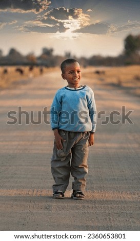 small african child walking on a dirt road at sunset in his way home Royalty-Free Stock Photo #2360653801