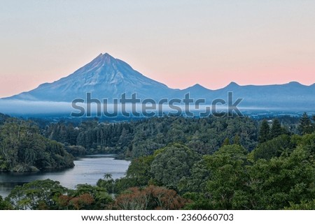 Peaceful scene at blue hour at dawn over Lake Mangamahoe on New Zealand’s North Island, surrounded by lush rainforest with the volcanic cone of Mt Taranaki in the background