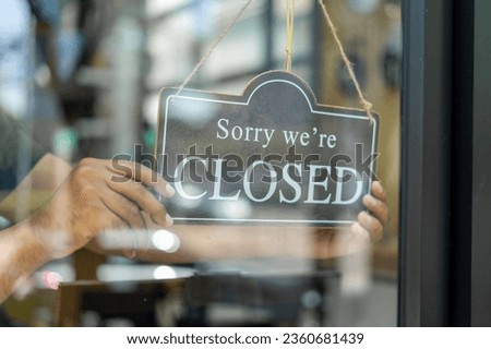 Shopkeeper setting closed sign at coffeeshop. Waiter in medical mask hanging card with closed lettering on cafe entrance door. Small business and startup concept.