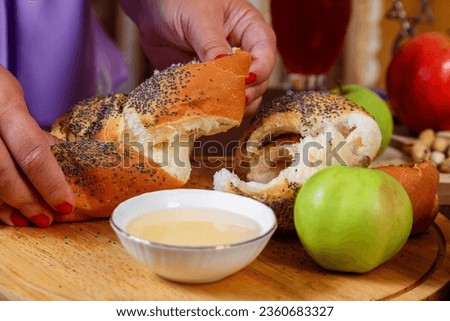 A woman's hand breaks the challah at the set table on the Jewish holiday Rosh Hashanah. Horizontal photo