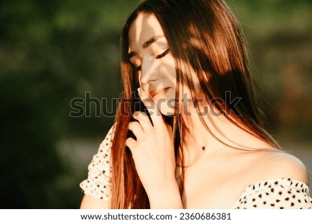 close-up portrait of a young woman on nature at sunset, woman face with shadow of foliage Royalty-Free Stock Photo #2360686381