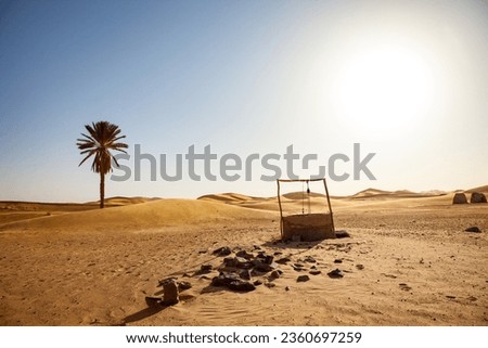 Old water well in the desert with palm tree and dunes in the background Royalty-Free Stock Photo #2360697259