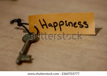 concept for a happy life using an old decorative key and a hand written tag attached by a black cord. Key to happiness, orange or brown paper written happiness word on it, positive attitude, mentality
