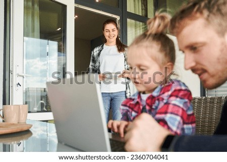 Positive man and little kid spending time at laptop computer together while pretty woman