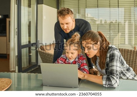 Adorable little girl looking at computer while sitting at table and spending time with her parents